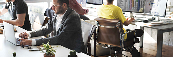 Office workers sitting at desks and using various types of devices and endpoints.