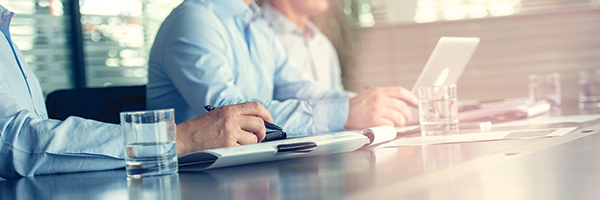 Homme assis à un bureau prenant des notes avec un autre homme travaillant sur un ordinateur portable assis à côté de lui.
